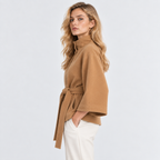Side view of a woman wearing a camel brown cape coat with wide sleeves and waist belt
