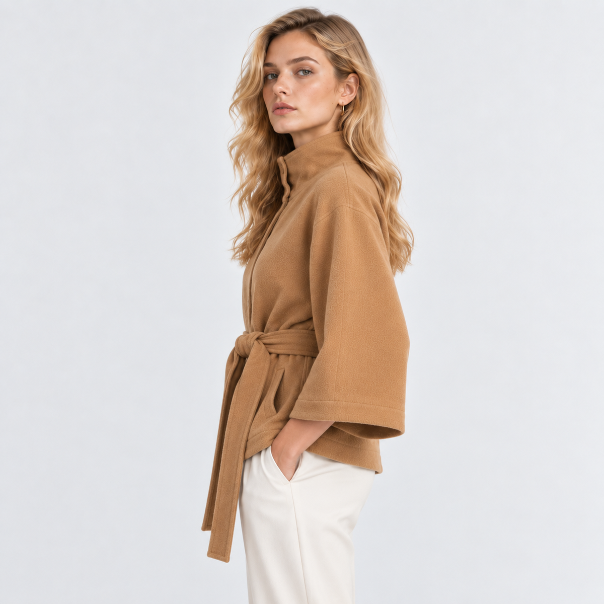 Side view of a woman wearing a camel brown cape coat with wide sleeves and waist belt
