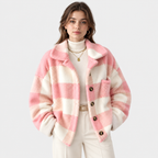 A woman wearing a pink and off-white checkered fuzzy cardigan over a cream turtleneck and cream pants, photographed against a light gray studio background.