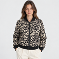 A woman wearing a leopard-print bomber jacket with black ribbed trim and a black front zipper, paired with cream pants, against a light gray studio background.