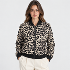 A woman wearing a leopard-print bomber jacket with black ribbed trim and a black front zipper, paired with cream pants, against a light gray studio background.