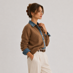 A woman models a brown knit cardigan with a blue denim collar and button placket, styled with cream trousers and a brown belt against a light gray studio background.
