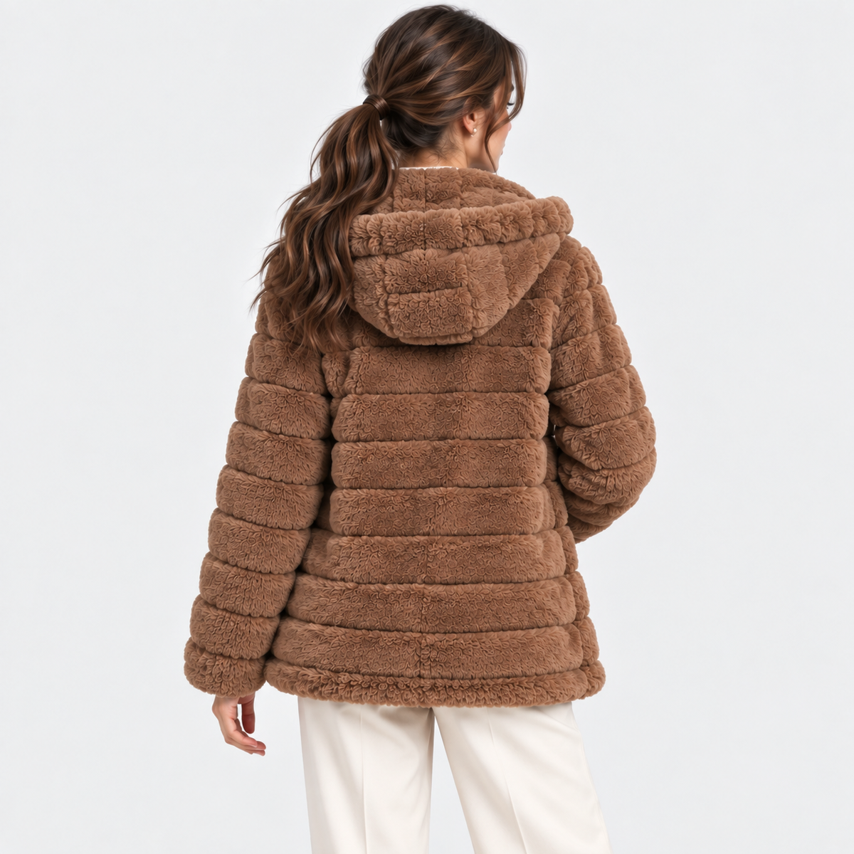 A woman shown from the back wearing a brown textured faux-fur hooded jacket with horizontal quilting, paired with off-white pants, against a plain light gray studio background.