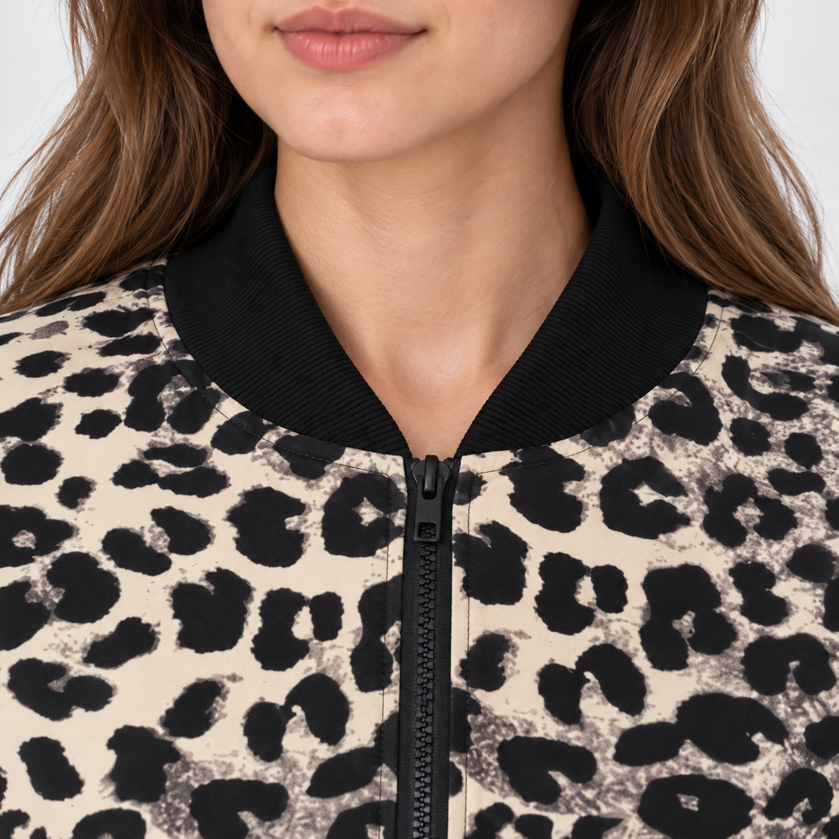 Close-up of a person wearing a leopard-print bomber jacket with a black ribbed collar and black front zipper.