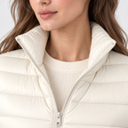 Close-up of a woman wearing a cream-colored puffer jacket with a high collar over a ribbed cream sweater.