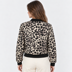 A woman shown from the back wearing a beige and black leopard-print bomber jacket with black ribbed collar, cuffs, and hem, paired with cream pants, against a light gray studio background.