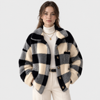 A woman models a black and cream checkered fuzzy cropped jacket over a cream turtleneck and cream trousers, against a light gray studio background.
