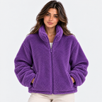 A woman wearing a purple sherpa fleece zip-up jacket with a high collar, shown against a plain light gray studio background.