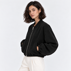 Side view of a woman wearing a black zip-up bomber jacket with white pants