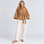 Woman wearing a camel brown cape coat with white trousers and ankle boots