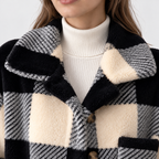 Close-up of a person wearing a black, cream, and gray plaid fuzzy coat over a cream ribbed turtleneck sweater.