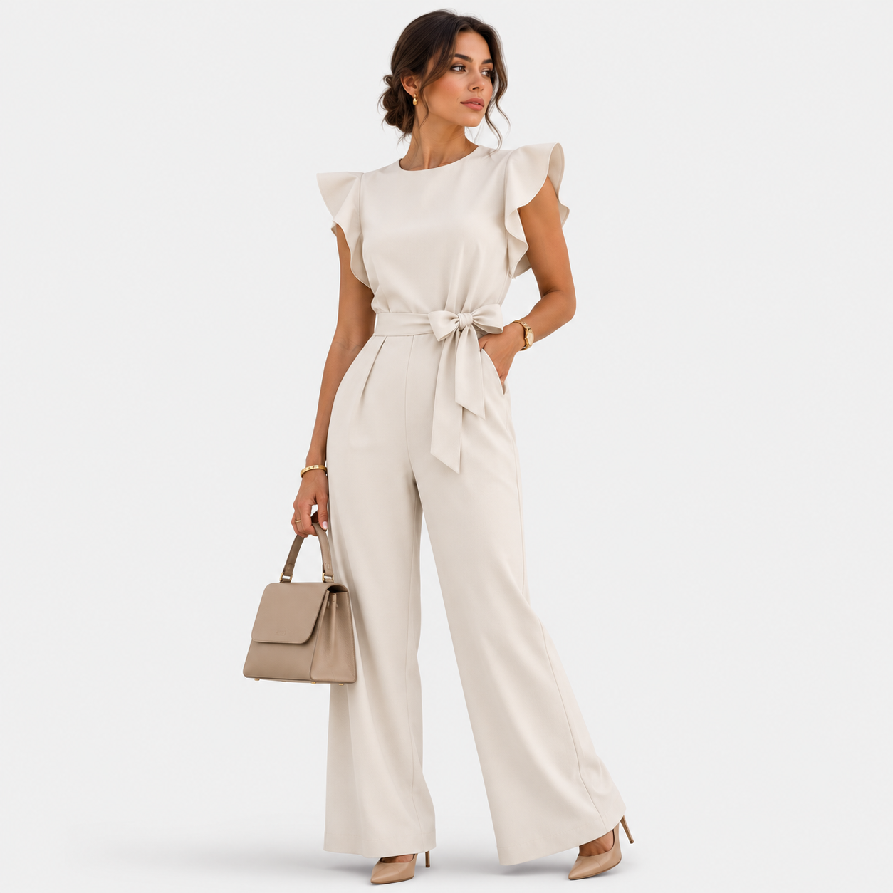 A woman models a cream-colored ruffled sleeve jumpsuit with a matching waist tie, paired with a beige handbag and nude heels, against a light gray studio background.
