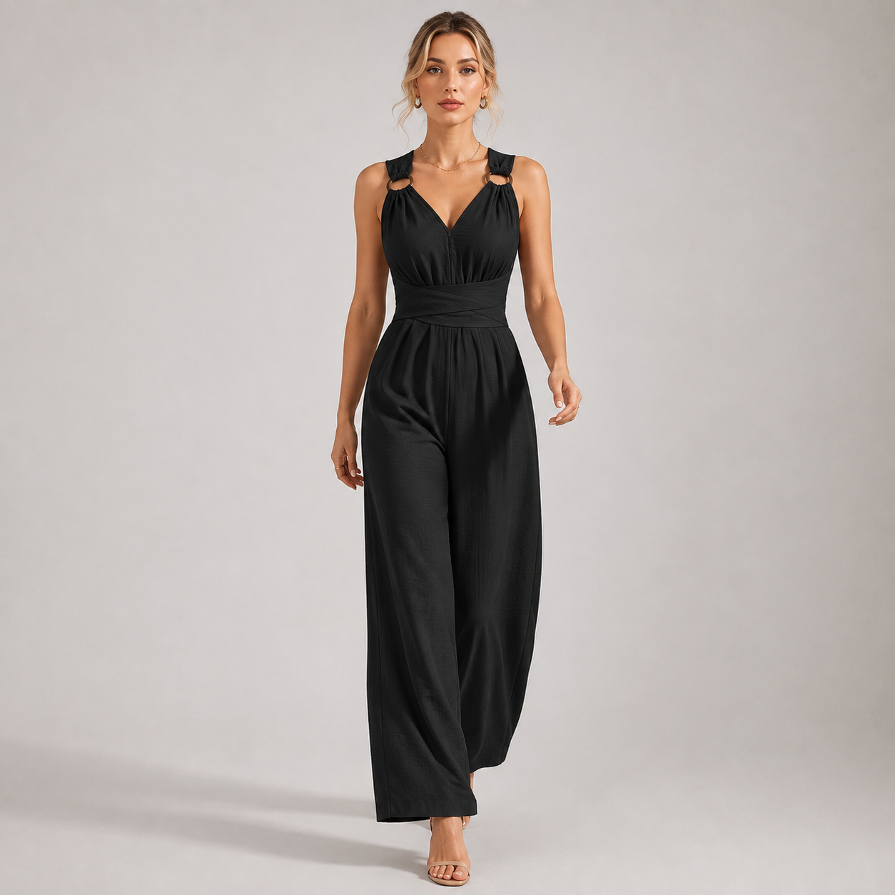 A woman modeling a black sleeveless jumpsuit with cutout shoulder details, a V-neckline, and wide-leg pants against a plain light gray studio background.