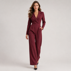 A woman modeling a long-sleeve burgundy wrap-style jumpsuit with wide legs and a matching waist belt, photographed against a plain light gray studio background.