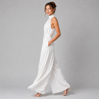 A woman modeling a white sleeveless high-neck wide-leg jumpsuit against a solid gray studio background.