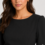 Close-up of a woman wearing a black long-sleeve top with structured shoulders and a boat neckline, shown against a light gray background.