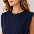 Close-up of a woman wearing a sleeveless navy blue top with a round neckline, shown against a light neutral background.