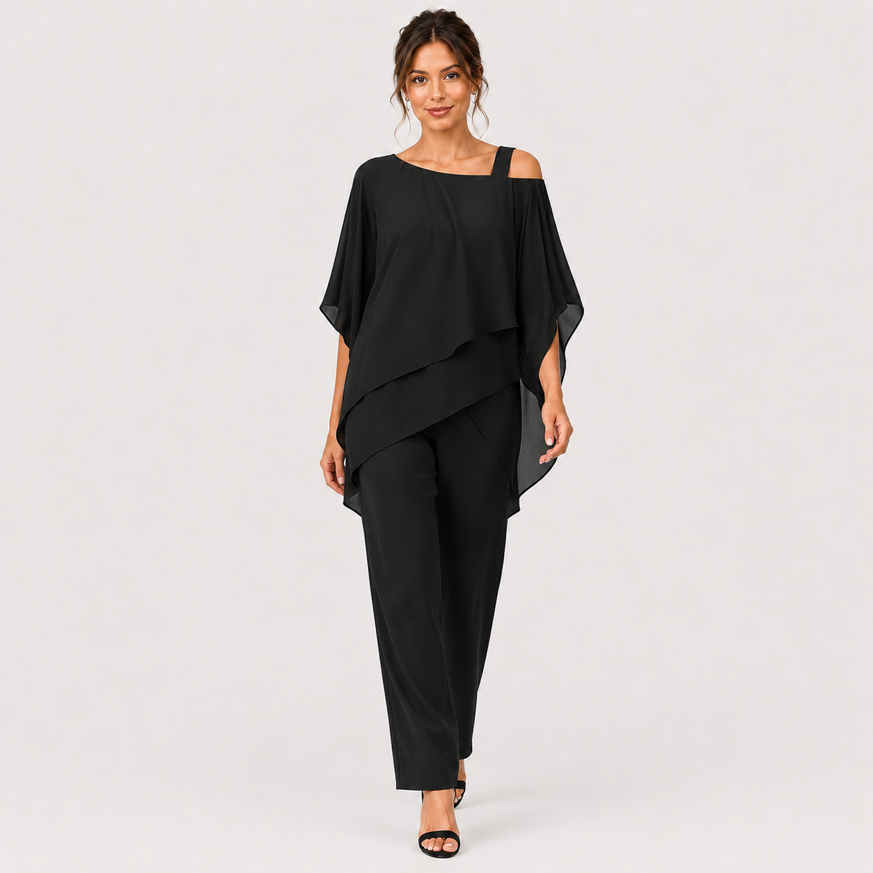 A woman modeling a black two-piece outfit consisting of a draped cold-shoulder top and matching wide-leg trousers, photographed against a plain light gray studio background.