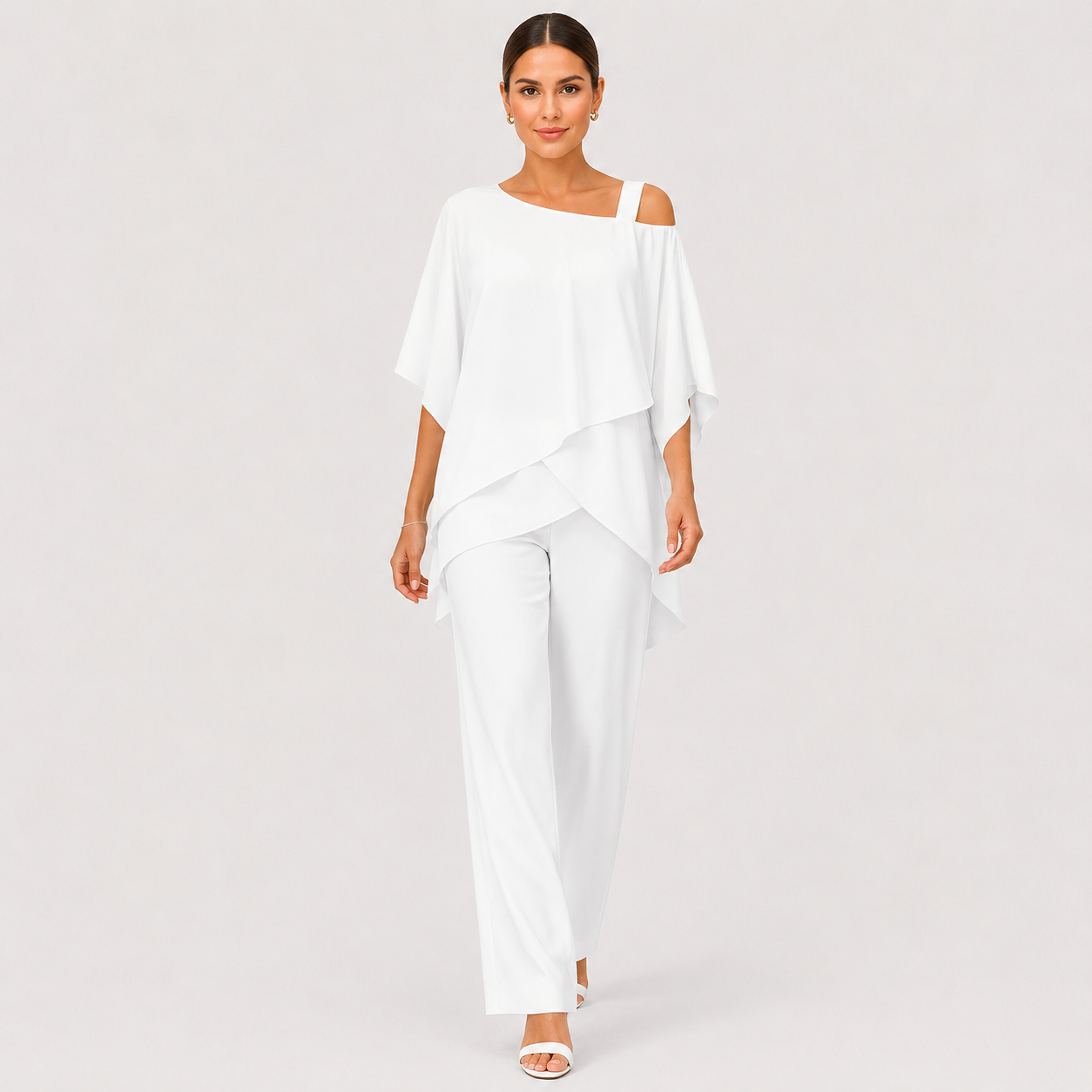 A woman modeling a white two-piece outfit consisting of a draped cold-shoulder top and matching wide-leg pants, photographed against a light gray studio background.