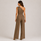 A woman wearing a brown one-shoulder wide-leg jumpsuit, shown from the back against a neutral light gray studio background.