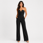 A woman modeling a black strapless wide-leg jumpsuit with a sweetheart neckline and front pockets, standing against a light gray studio background.