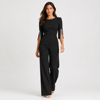A woman modeling a black three-quarter sleeve jumpsuit with pearl embellishments on the sleeve cuffs, photographed against a light gray studio background.