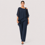A woman modeling a navy blue two-piece outfit consisting of a draped off-the-shoulder top and matching wide-leg trousers, holding a small matching navy clutch against a light gray studio background.
