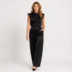 A woman modeling a black satin sleeveless top and matching wide-leg trousers against a light gray studio background.