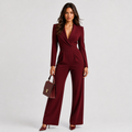 A woman modeling a deep burgundy wrap-style jumpsuit with long sleeves and wide legs, holding a matching burgundy handbag against a light gray studio background.
