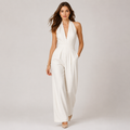 A woman modeling a white halter-neck jumpsuit with a deep V-neckline, defined waist seam, and wide-leg pants, set against a plain light gray studio background.