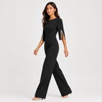 A woman modeling a black wide-leg jumpsuit with three-quarter sleeves and decorative pearl trim on the sleeve edges, photographed against a light gray studio background.