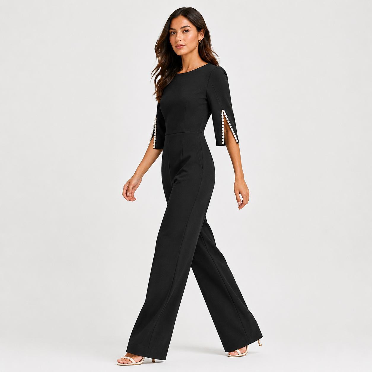 A woman modeling a black wide-leg jumpsuit with three-quarter sleeves and decorative pearl trim on the sleeve edges, photographed against a light gray studio background.