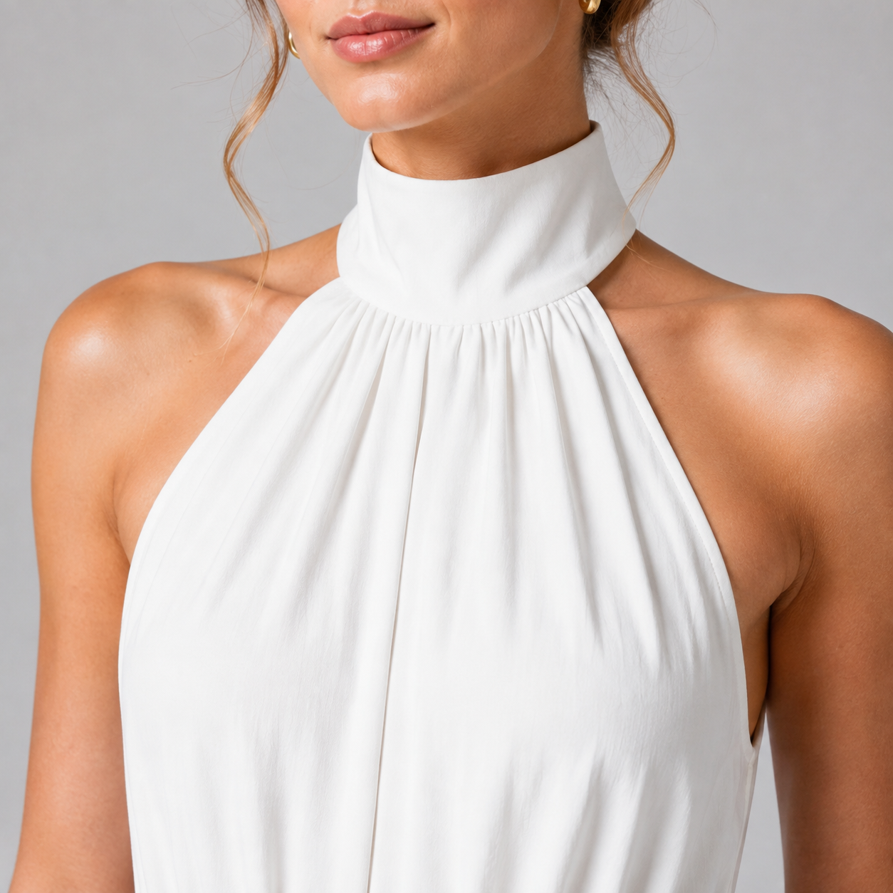 Close-up of a woman wearing a white high-neck halter top against a light gray studio background.