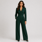 A woman modeling a dark green wrap-style jumpsuit with wide legs, standing against a plain light gray studio background.