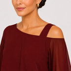 A close-up of a woman wearing a burgundy cold-shoulder top with wide straps and sheer long sleeves, paired with a gold hoop earring, against a light gray background.