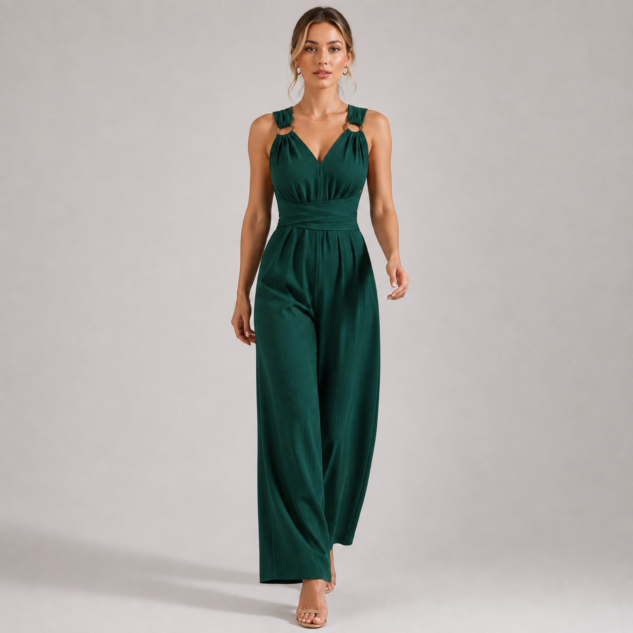 A woman modeling a dark green sleeveless jumpsuit with shoulder cutouts, a V-neckline, and wide legs against a plain light gray studio background.