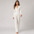 A woman modeling a white long-sleeve wrap-style jumpsuit with a defined waist and wide-leg trousers, photographed against a light gray studio background.