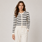 A woman modeling a black and white horizontally striped cardigan with gold buttons, paired with cream-colored trousers, against a neutral light gray background.