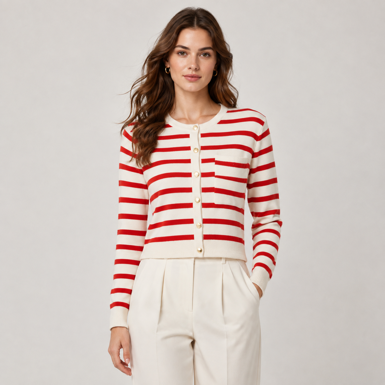 A woman modeling a red and cream striped cardigan with cream buttons, paired with cream trousers, against a light gray studio background.