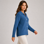 A woman wearing a blue ribbed knit button-front cardigan with a collar, paired with white pants, photographed against a plain light gray studio background.