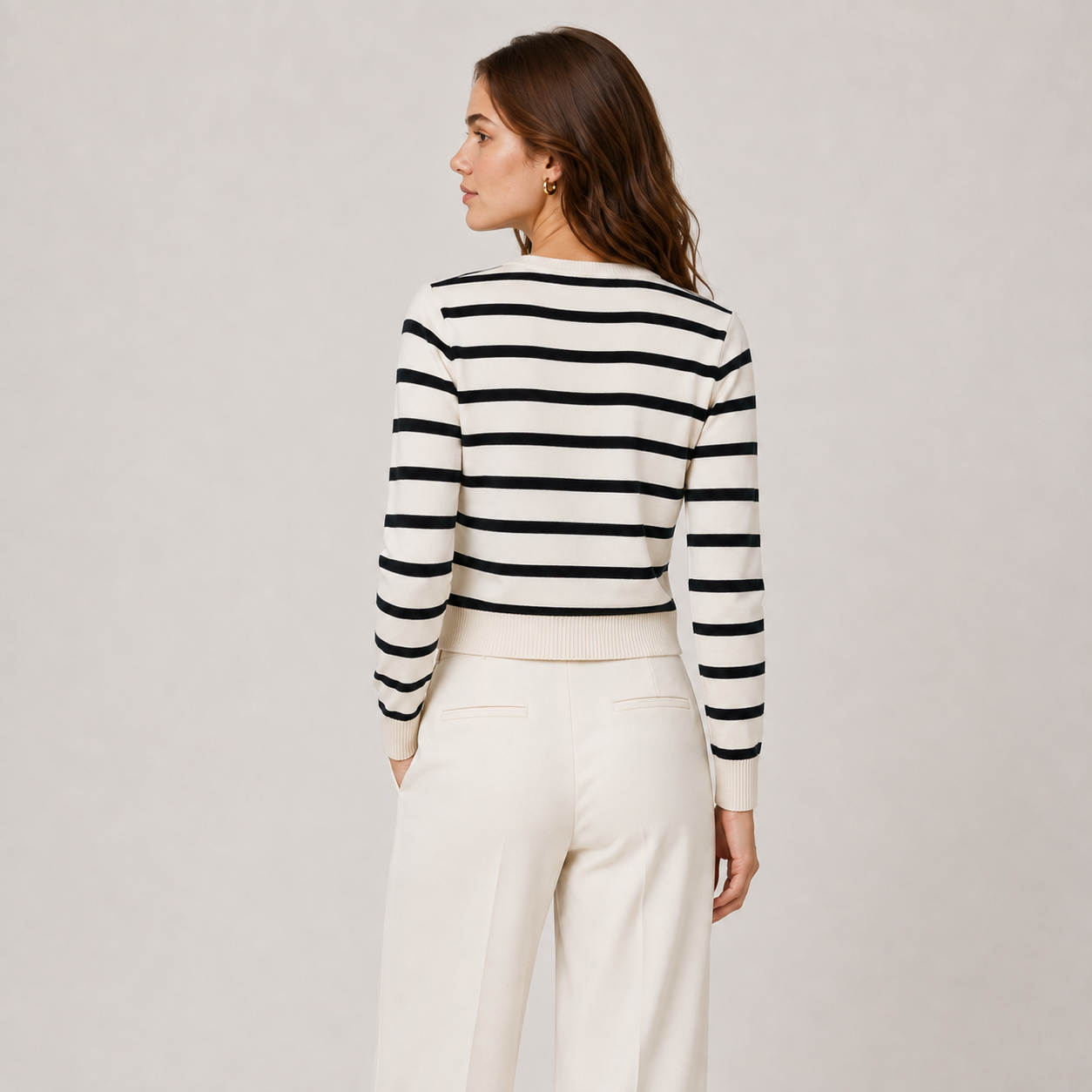 A woman shown from the back wearing a cropped knit sweater with horizontal black and off-white stripes, paired with off-white trousers, against a plain light gray studio background.
