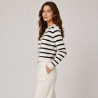A woman modeling a cropped, long-sleeve knit cardigan with horizontal black and off-white stripes, paired with off-white trousers, against a neutral light gray studio background.