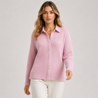 A woman modeling a light pink ribbed knit button-up cardigan sweater with a collar, paired with white pants, against a neutral light gray studio background.