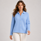 A woman modeling a light blue ribbed knit button-front cardigan sweater with a collar, paired with cream pants, against a plain light gray studio background.