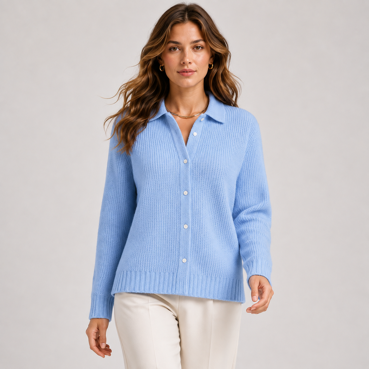 A woman modeling a light blue ribbed knit button-front cardigan sweater with a collar, paired with cream pants, against a plain light gray studio background.