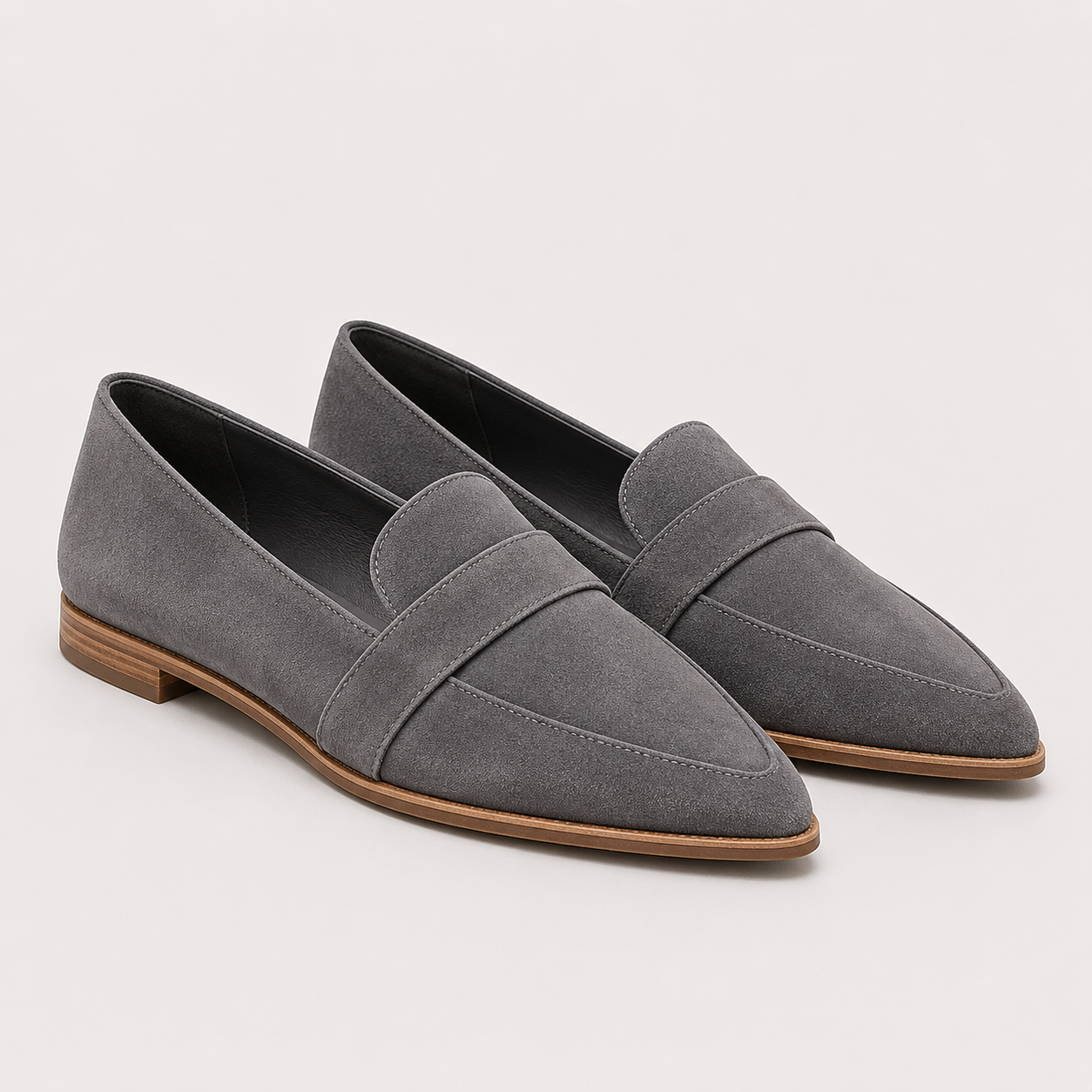 A pair of gray suede penny loafers with pointed toes and low brown block heels, shown on a light gray background.
