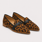 A pair of pointed-toe loafers in a brown and black leopard print with a wide black leather strap across the instep, shown on a light gray background.
