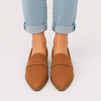 A pair of women's brown suede penny loafers worn with light-wash cuffed jeans, shown from the front against a plain light gray background.
