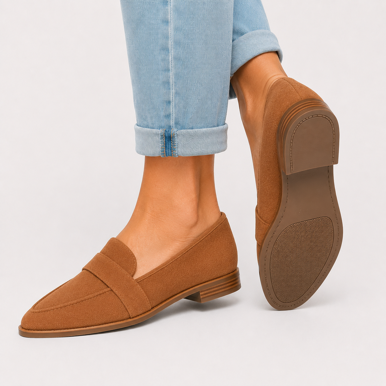 A pair of women's tan suede penny loafers shown on a model's feet, with one shoe facing forward and the other angled to show the sole, against a light gray background.