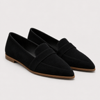 A pair of black suede penny loafers with pointed toes and low brown block heels, photographed on a light gray studio background.